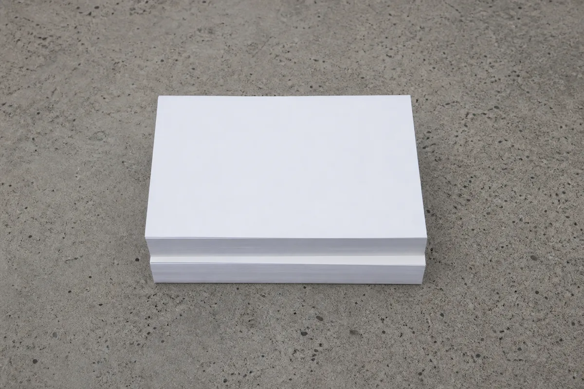 Deux rames de papier blanc empilées à plat sur une dalle de béton brut