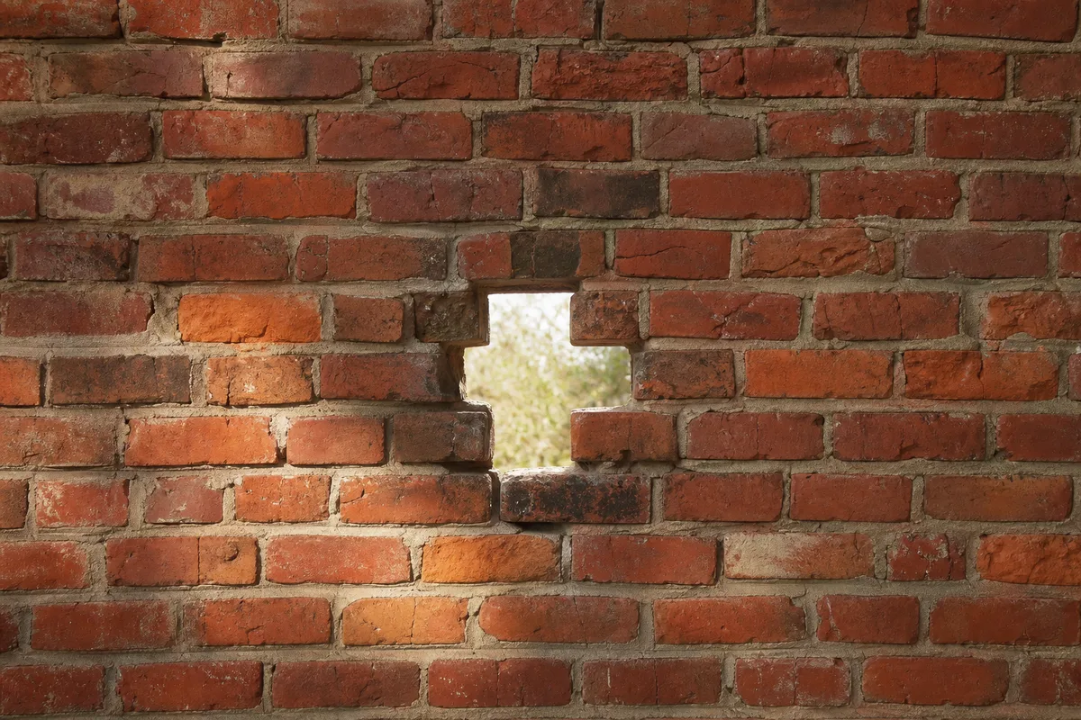 Mur de briques anciennes présentant une brèche par laquelle passe la lumière du jour