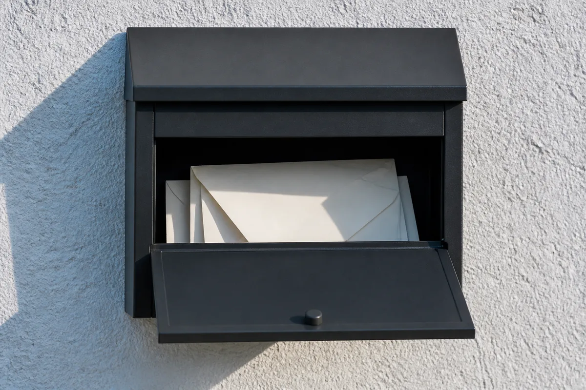 Boîte aux lettres métallique mate ouverte sur un mur crépi clair